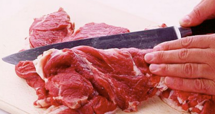 Close-in image of meat being sliced by a large knife